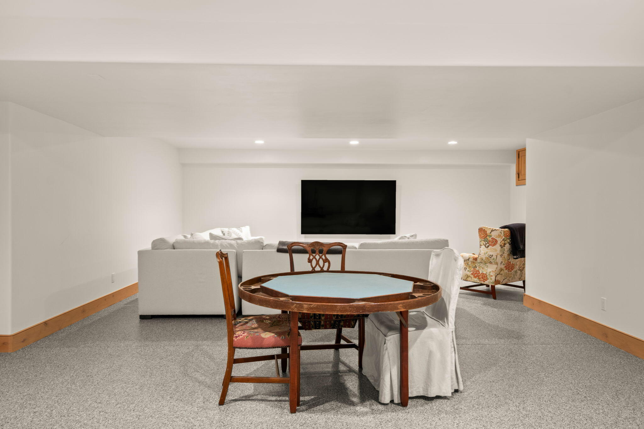 Furnished recreation room with a round game table, white sectional sofa, and wall-mounted television.