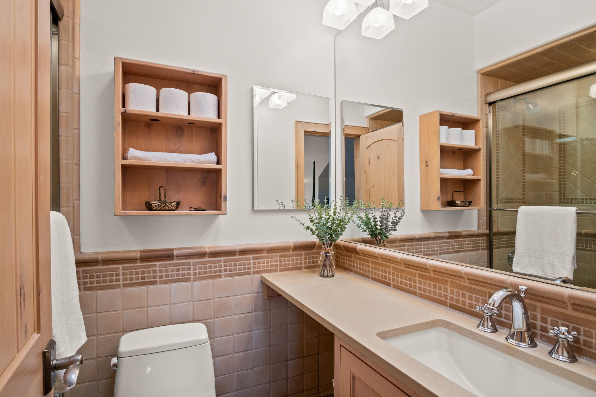 Bathroom with a long tiled vanity, wood towel shelves, a large mirror, and a glass-enclosed shower.