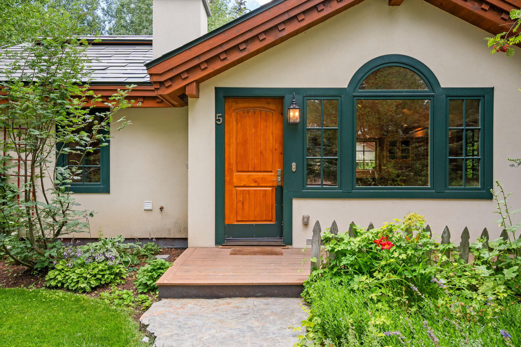 Home entrance with a wooden door, dark green arched window trim, and a flower-filled garden path.