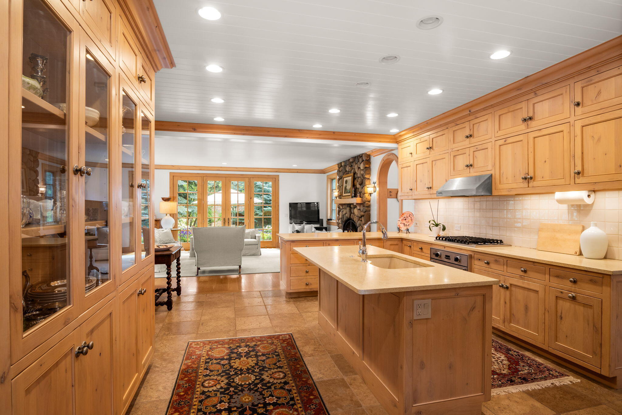 Wood-paneled kitchen with a large island opening to a living room with a stone fireplace.