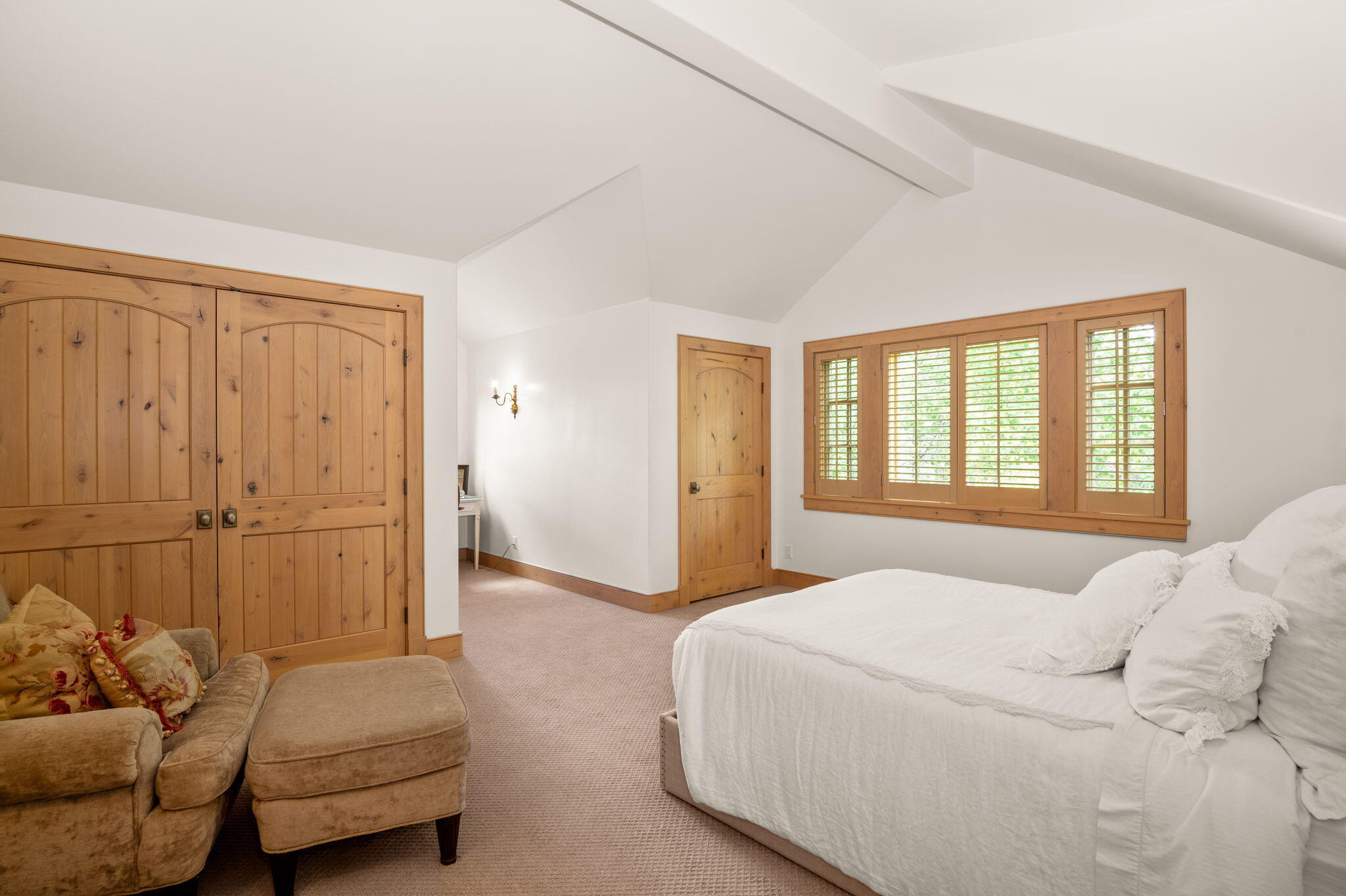 Bedroom with a white bed, wood-paneled doors, and a wide shuttered window.