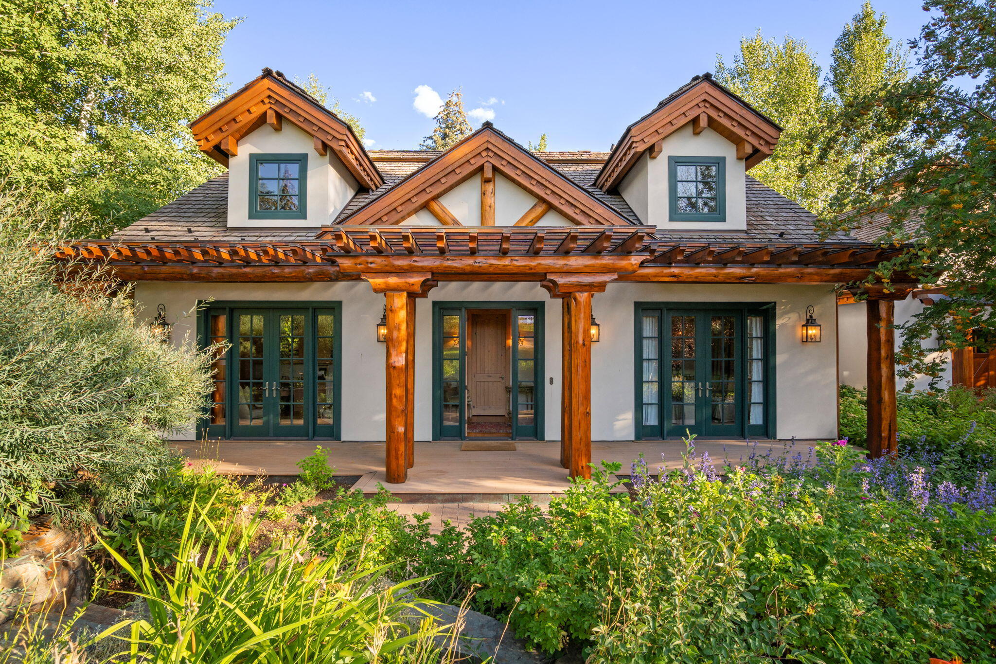 Two-story home with a timber porch, green-framed windows, and a lush flower garden.