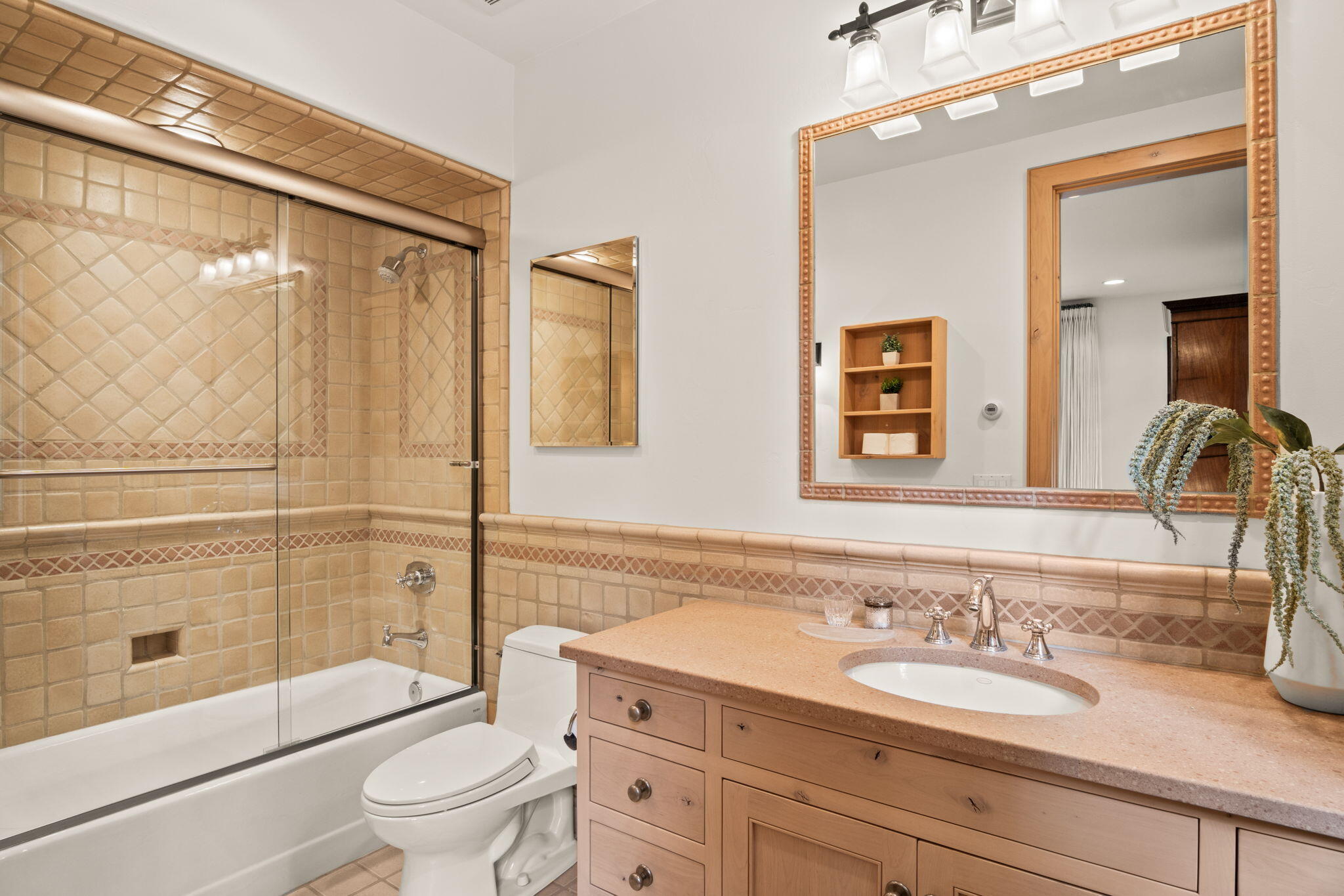 Bathroom with tan tiled tub and glass shower beside a wood vanity and large mirror.