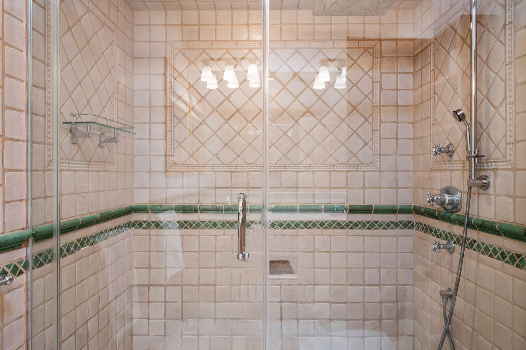 Tiled shower with a glass enclosure, chrome fixtures, and green accent tiles.
