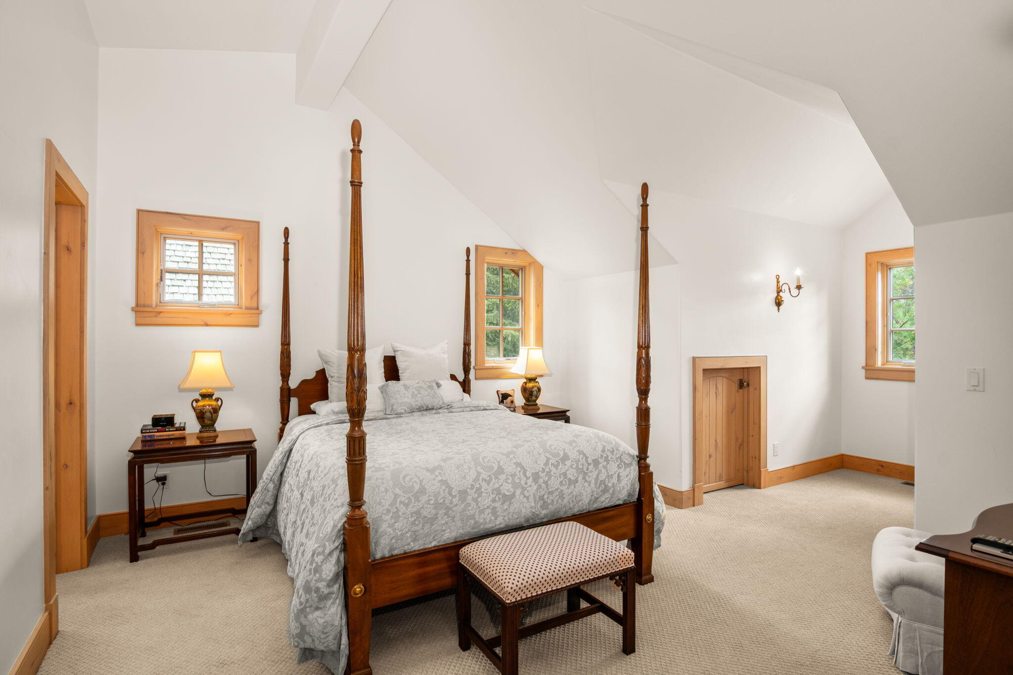 Bedroom with a wooden four-poster bed, patterned gray bedding, and a high sloped ceiling.