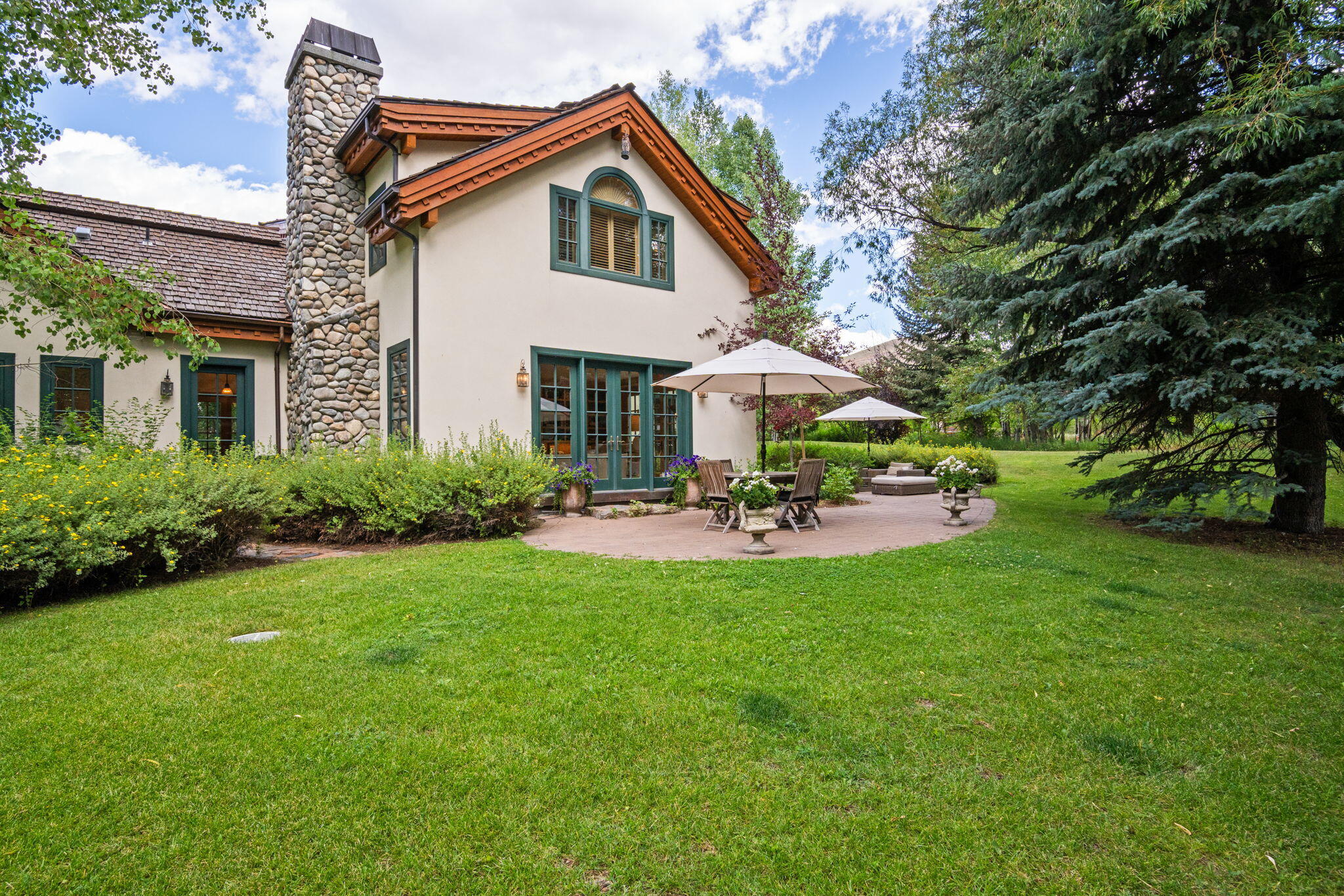 Home with a stone chimney and furnished patio opening onto a broad green lawn.