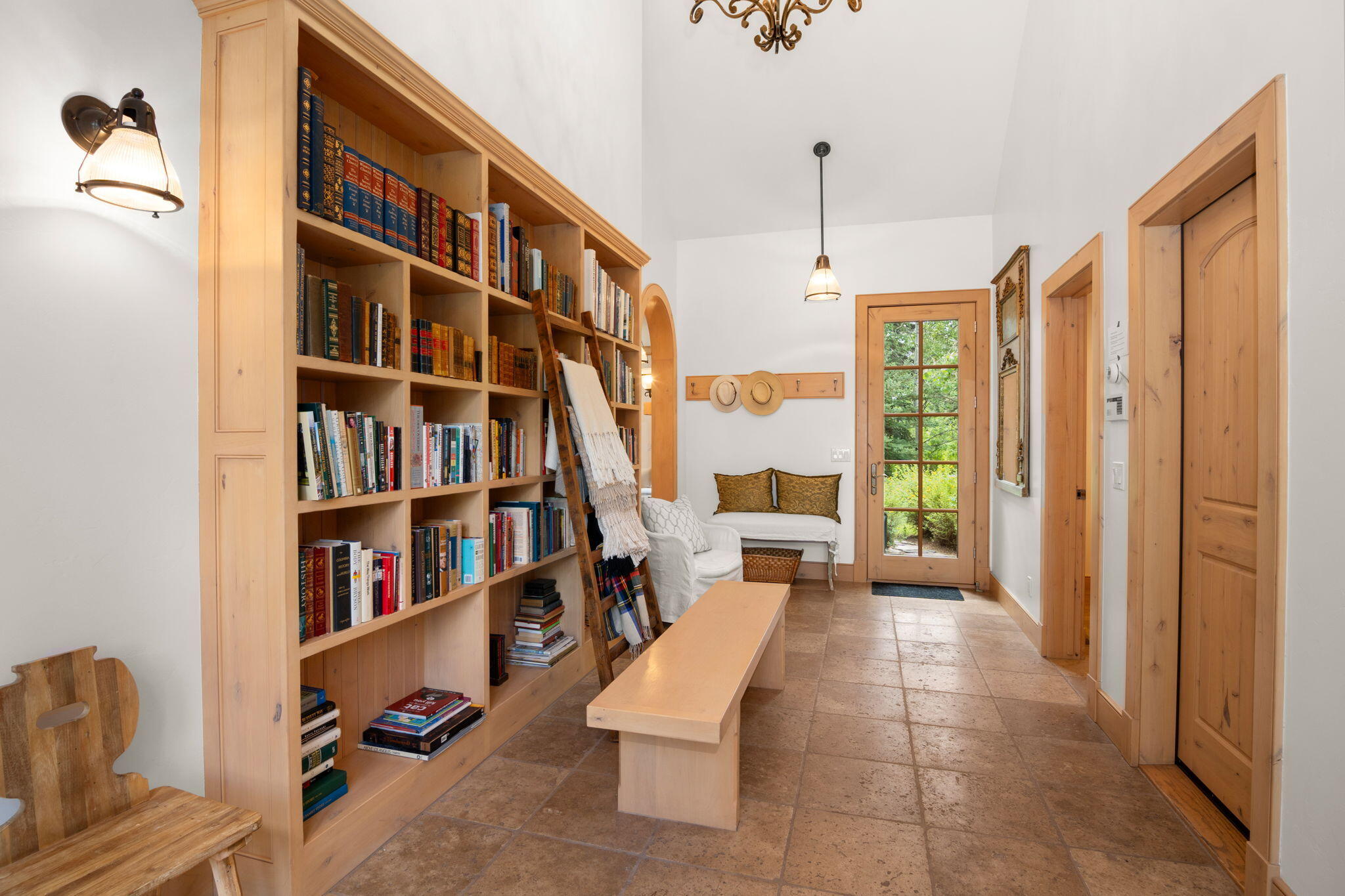 Hallway with built-in bookshelves and rolling ladder, tiled floor, and a glass-paneled door.