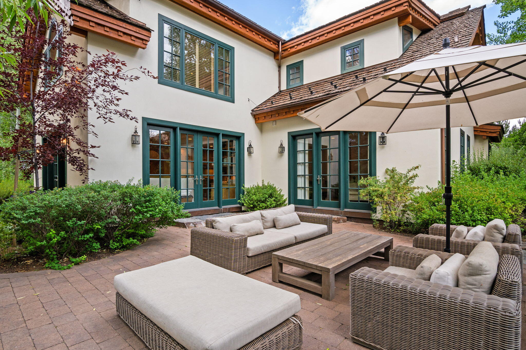 Outdoor patio with wicker lounge seating and umbrella beside a two-story stucco home.