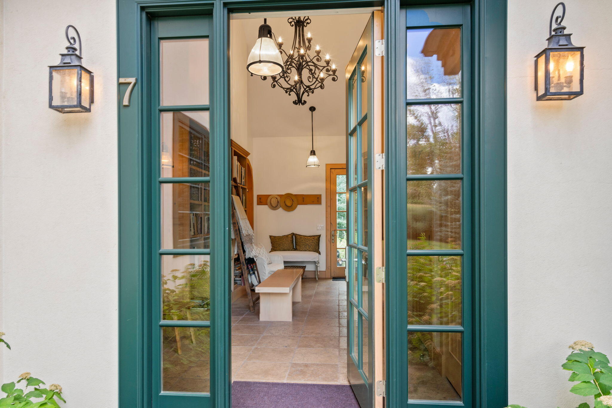 Open teal-framed front door reveals a tiled entryway with a bench and ornate chandeliers.