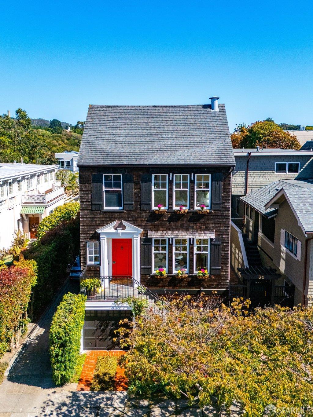 Dark-shingled house with a steep roof, red front door, and landscaped front garden.