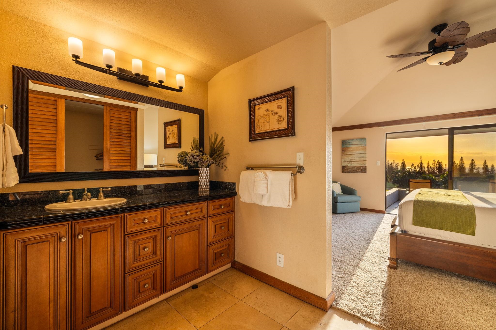 Bathroom vanity opens onto a bedroom with sliding glass doors and a golden-hour view of trees.