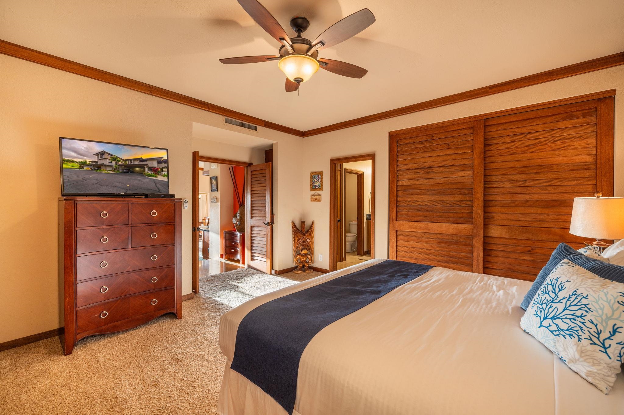 Furnished bedroom with a king bed, wood louvered closet doors, and a ceiling fan.