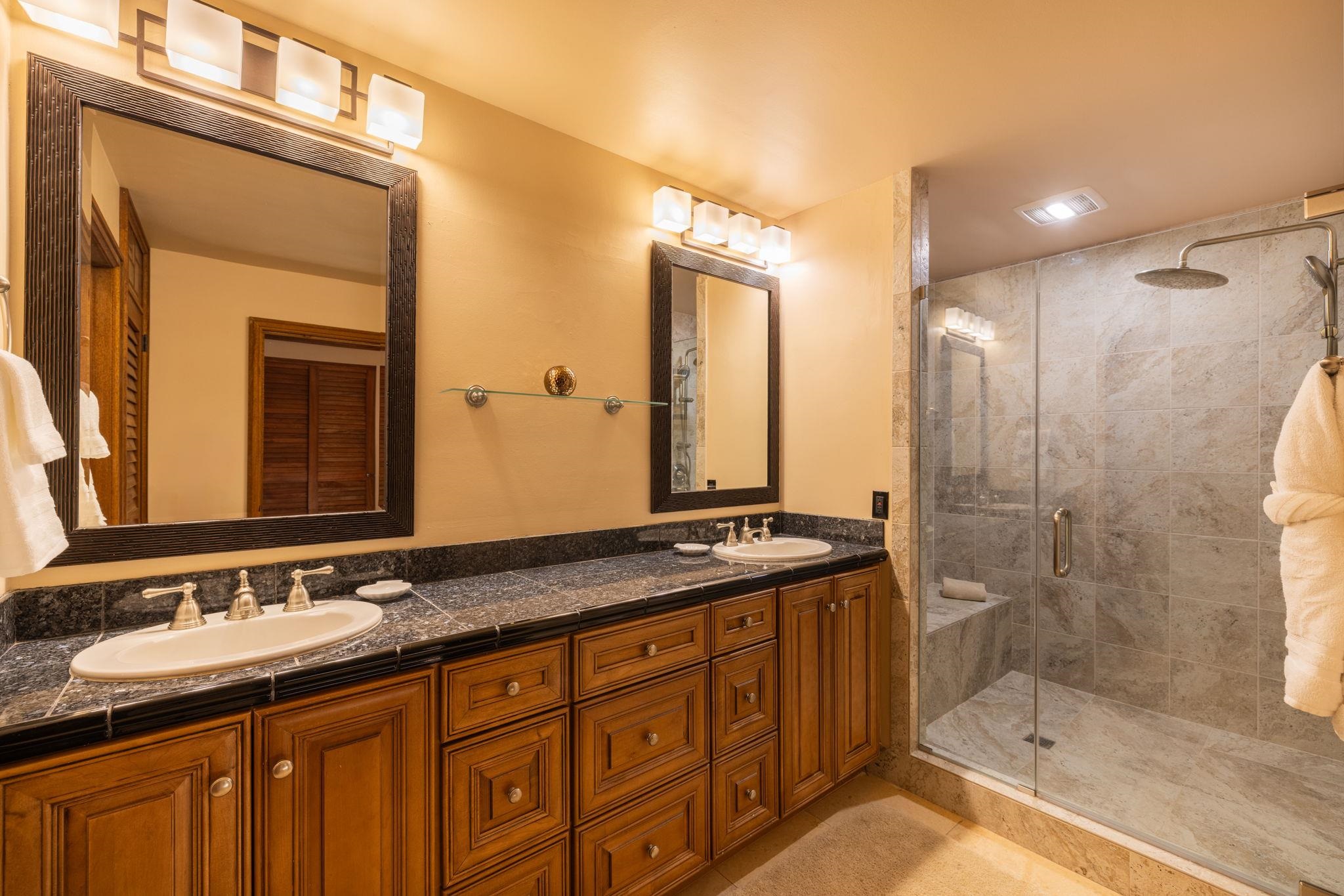 Bathroom with a double-sink wood vanity and glass-enclosed tiled shower.