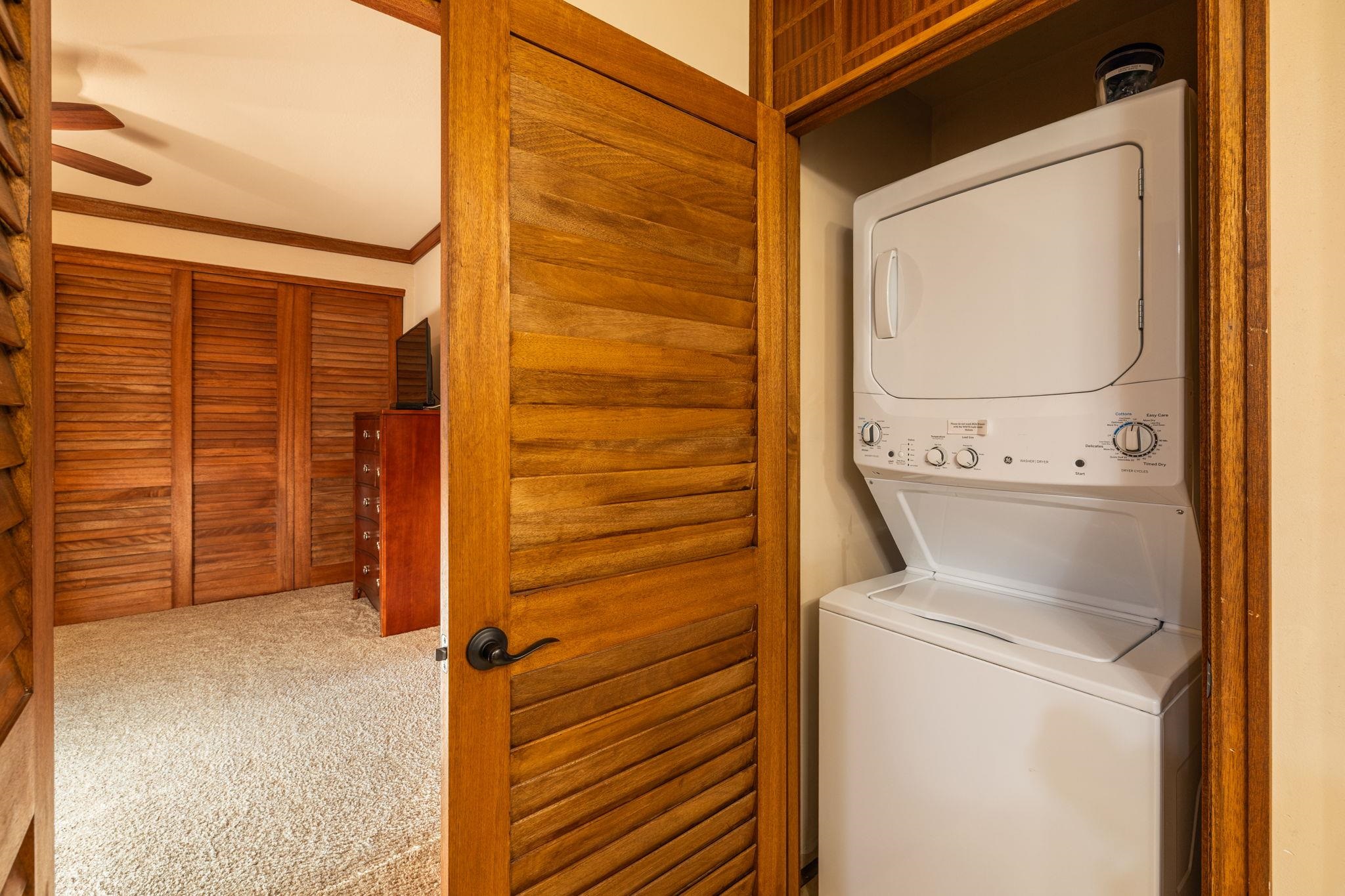 Laundry closet with a stacked washer and dryer behind an open wooden louvered door.