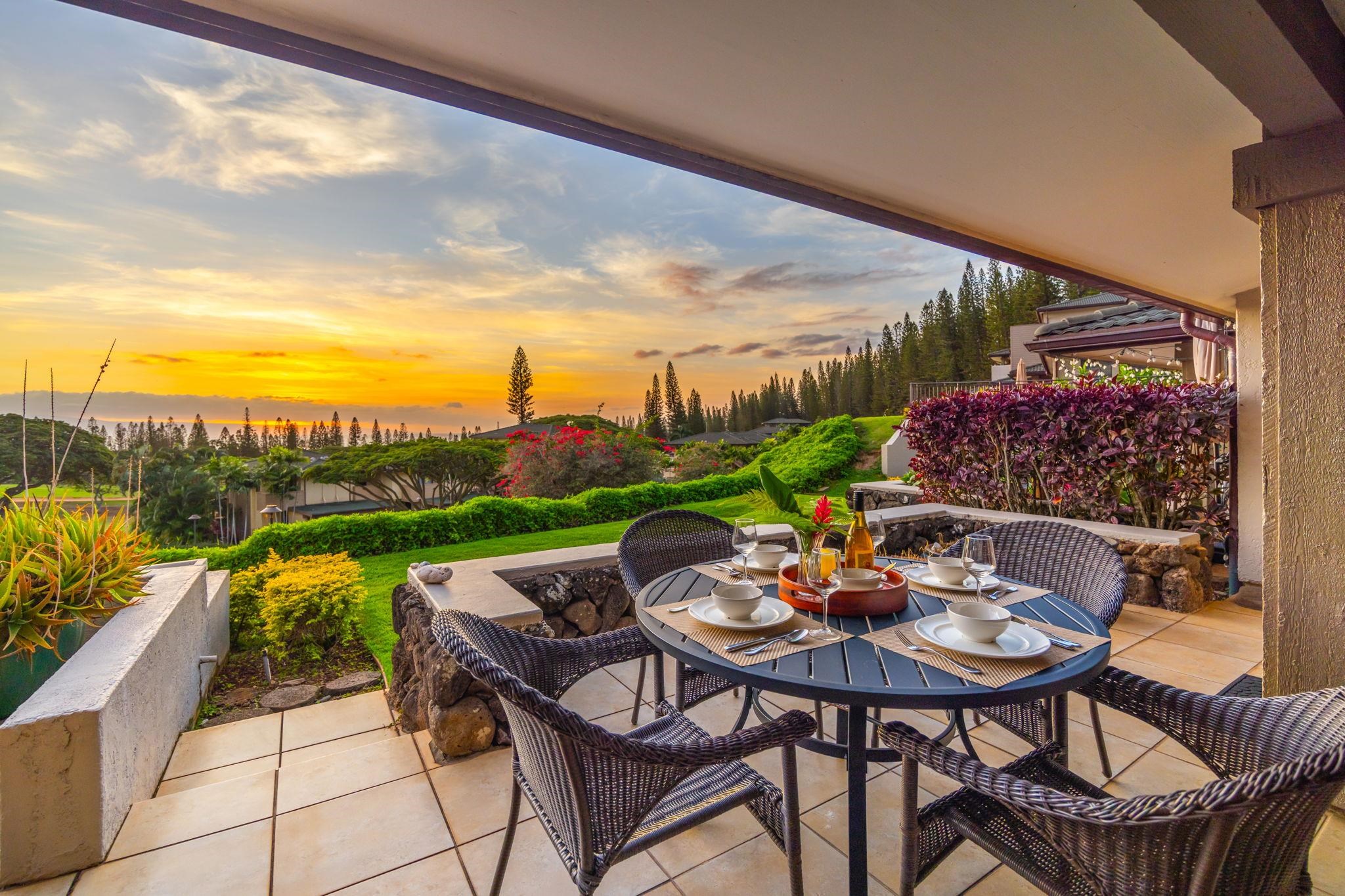 Covered patio dining area overlooking a landscaped garden and ocean at sunset.