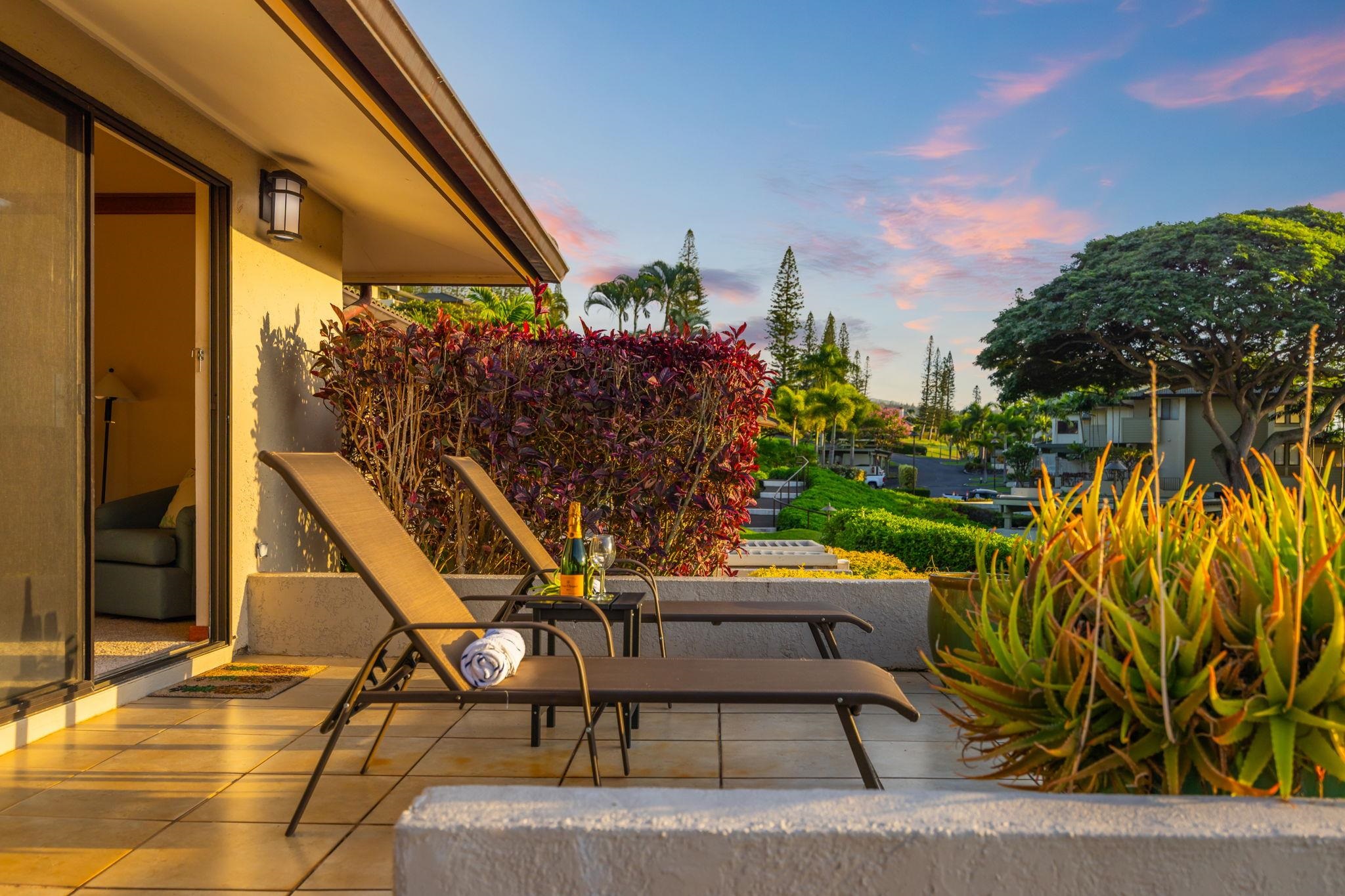 Condo patio with chaise lounges and tropical plants overlooking landscaped grounds and neighboring buildings.
