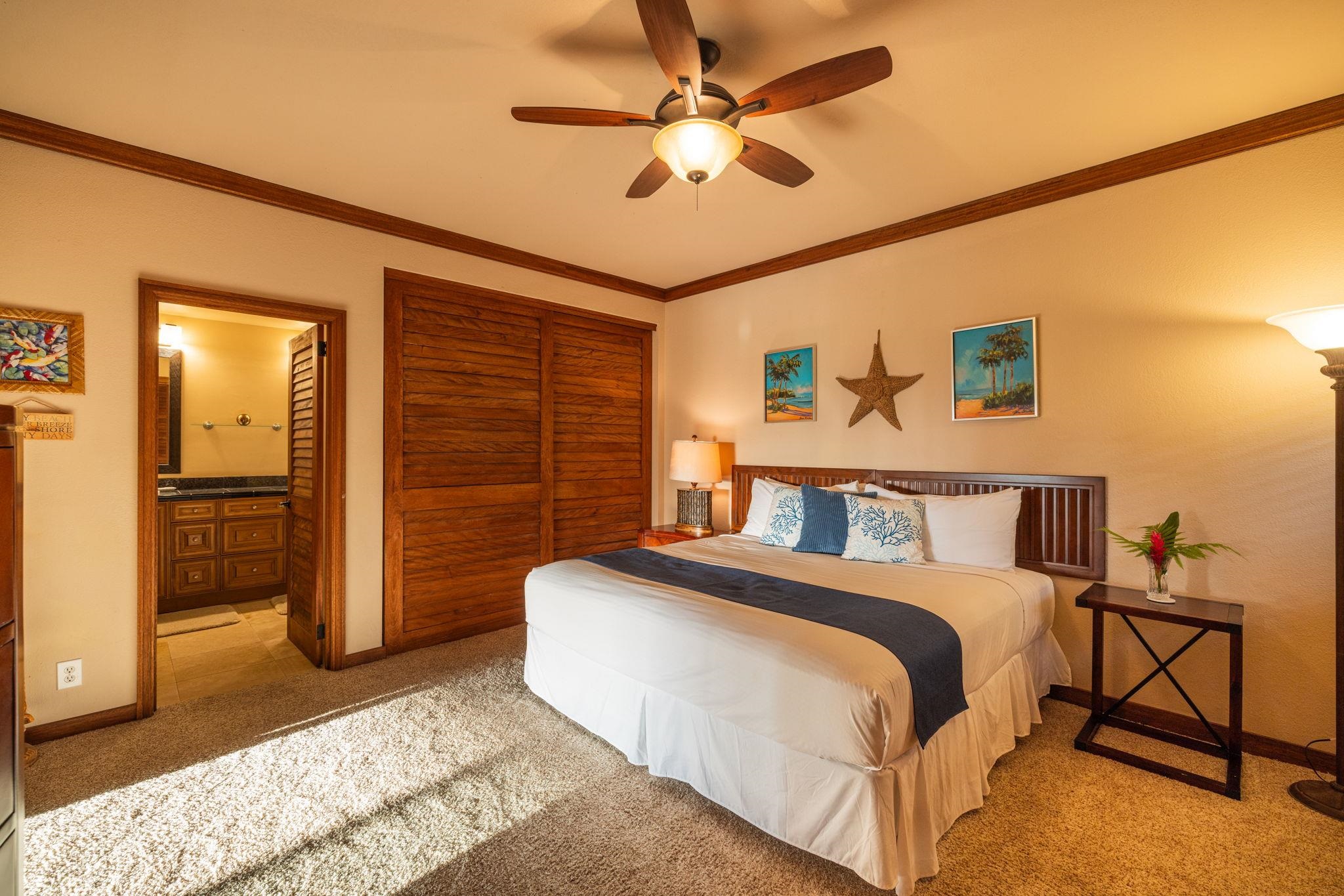 Bedroom with a white-and-navy bed, dark wood closet doors, and an open bathroom doorway.