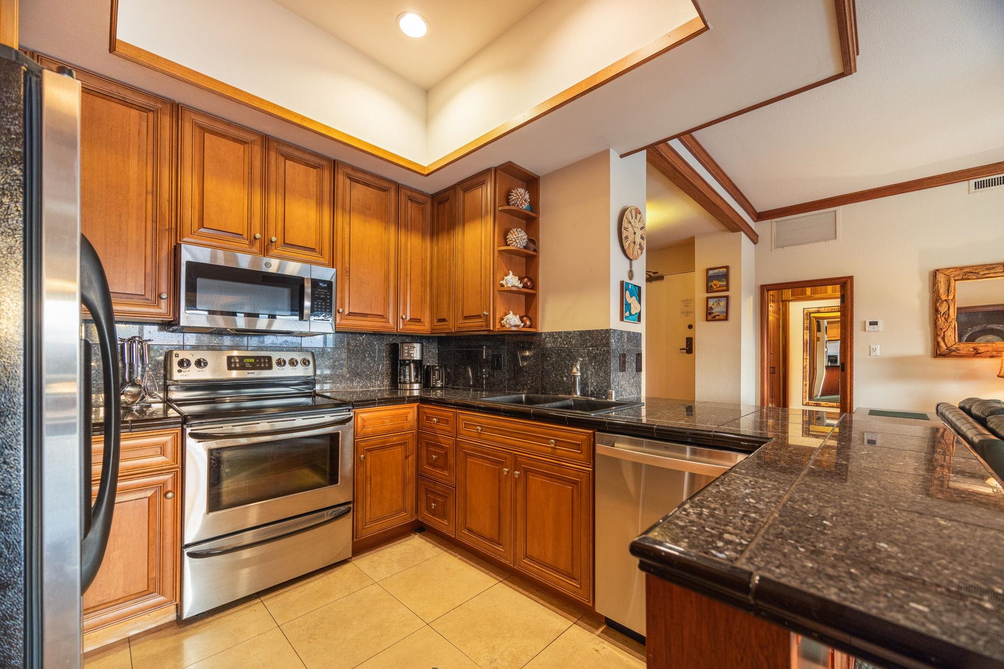 Kitchen with wood cabinetry, dark granite counters, stainless steel appliances, and a breakfast bar.