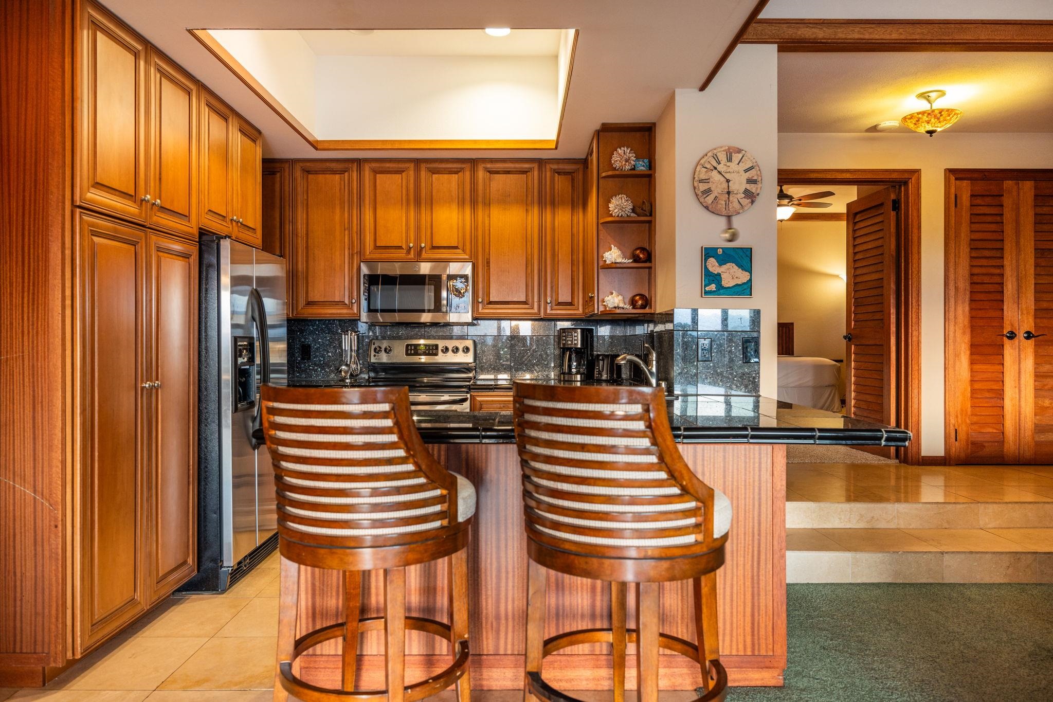 Kitchen with extensive wood cabinetry, stainless appliances, and a breakfast bar with two stools.