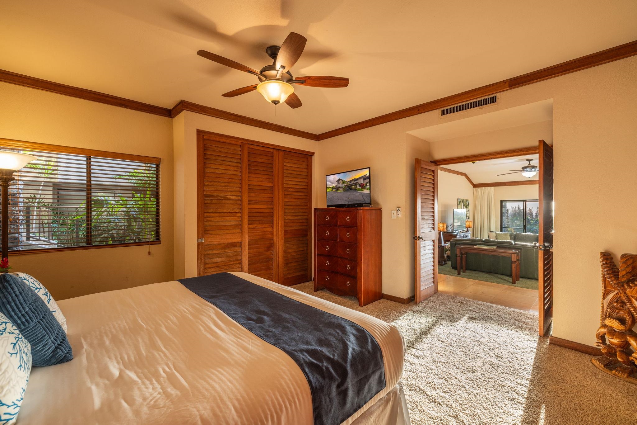 Bedroom with wooden louvered closet doors and open doors to an adjoining living room.