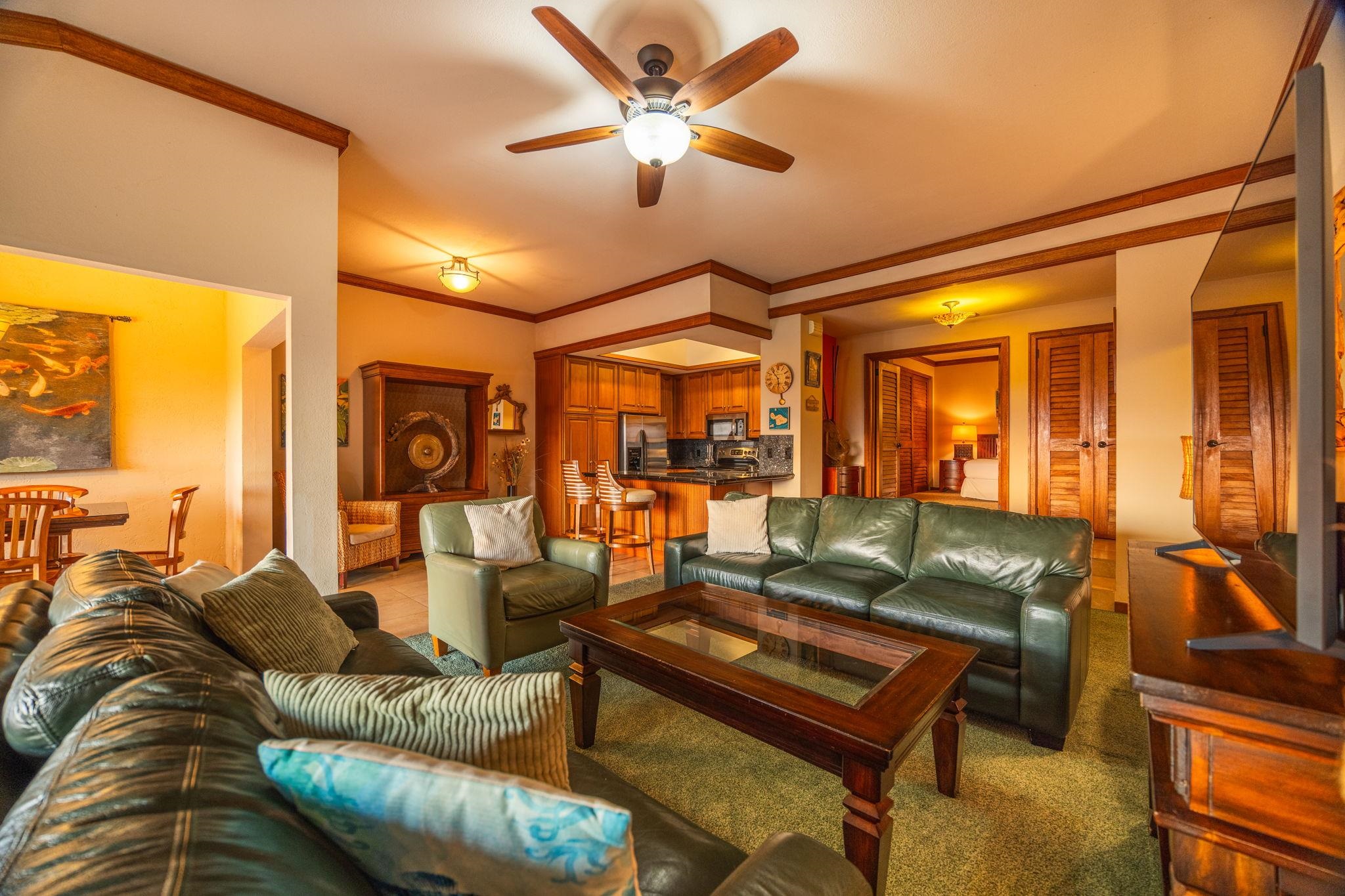 Furnished living room with green leather sofas, wood coffee table, ceiling fan, and open kitchen.