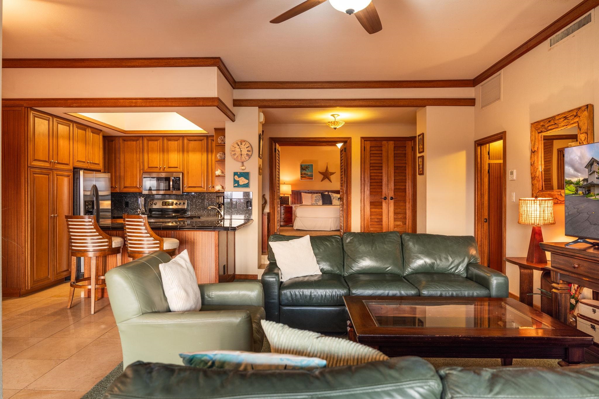Open-plan living room with green leather sofas, wood cabinetry, and a bedroom beyond.