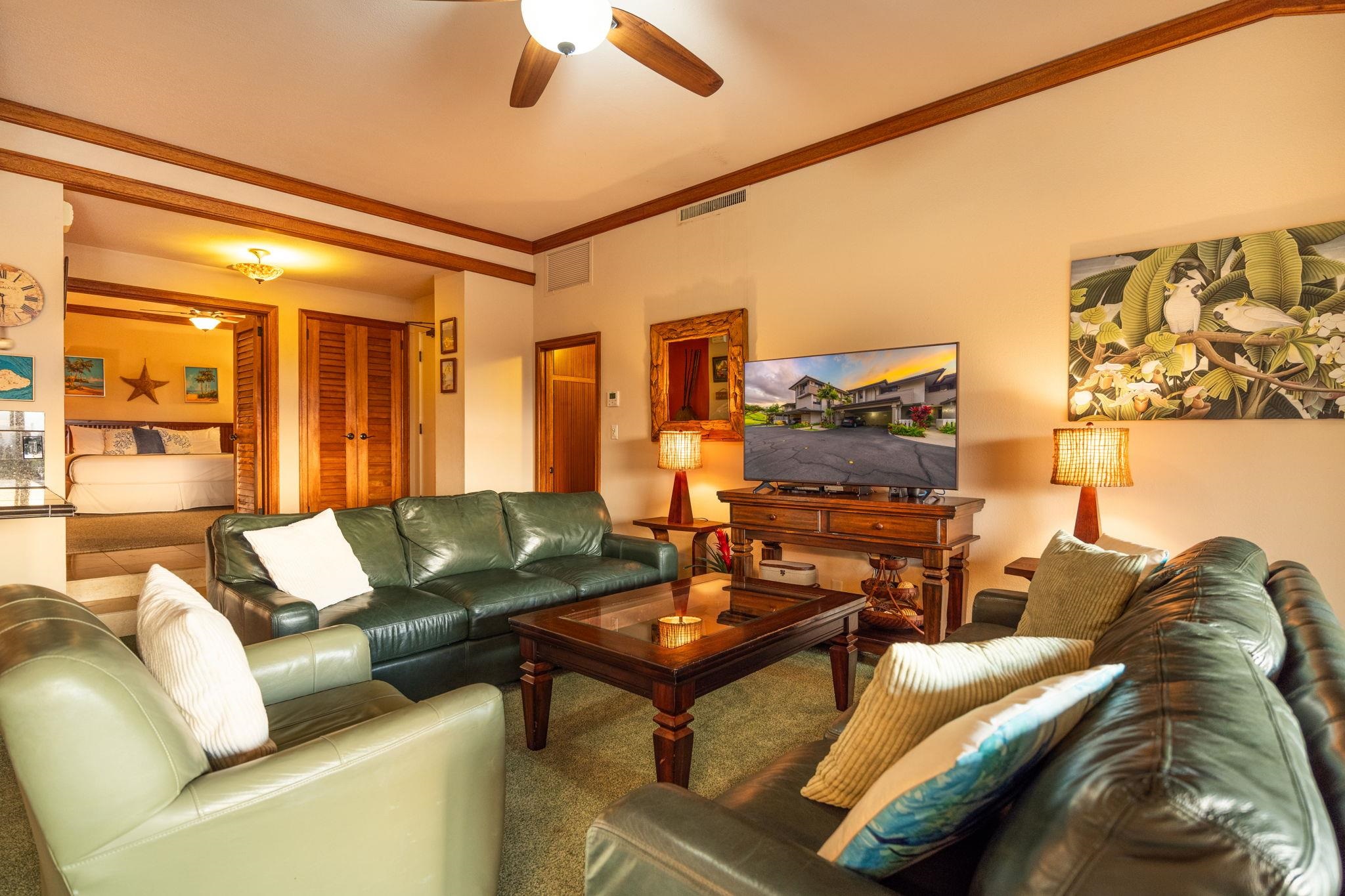 Furnished living room with green leather sofas, dark wood furniture, and an adjoining bedroom.