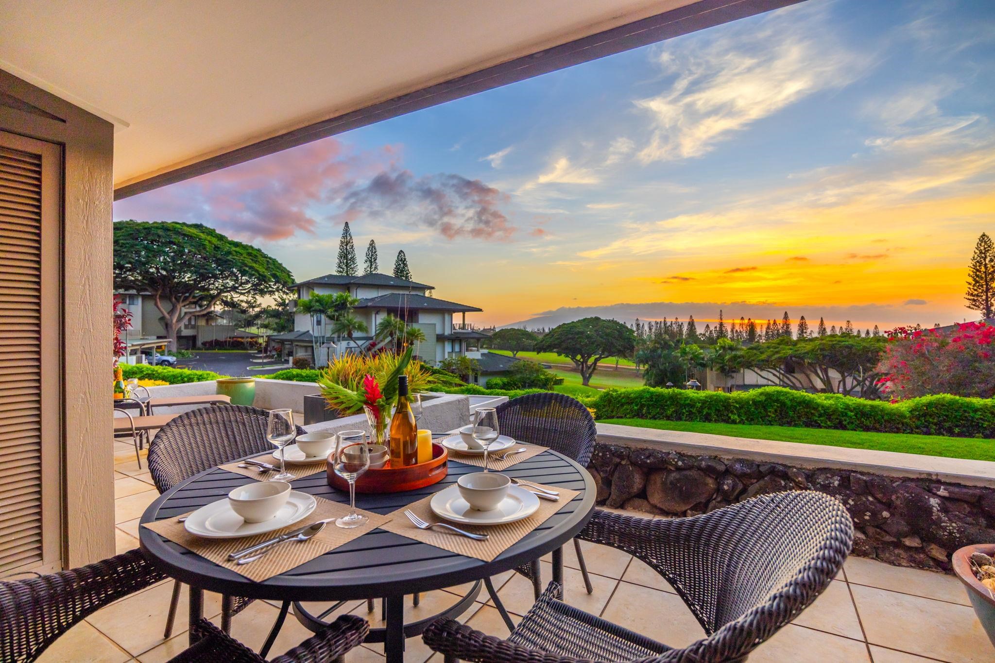 Patio dining table overlooking landscaped grounds and the ocean at sunset.