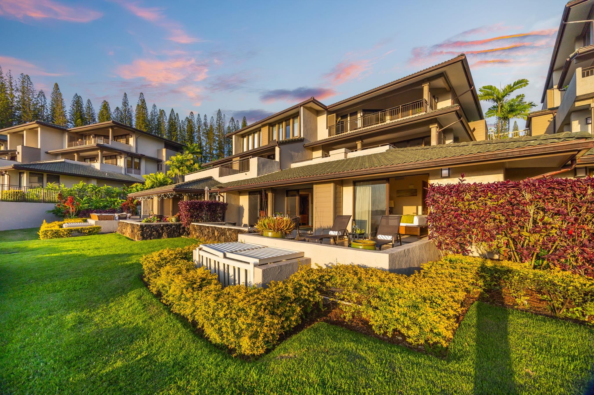 Multi-level condominium with furnished patios, tropical landscaping, and a broad lawn at golden hour.