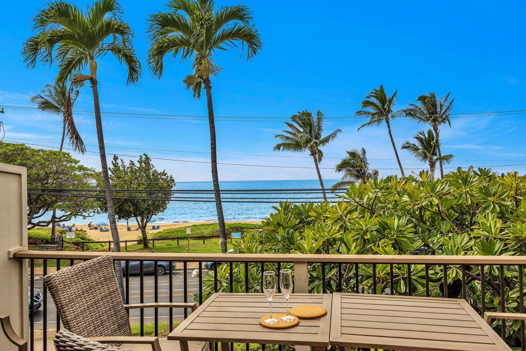 Balcony with a table and wicker chair overlooking palm trees, beach, and ocean.