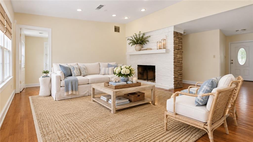 Staged living room with a white sofa, wicker chairs, and a white brick fireplace.