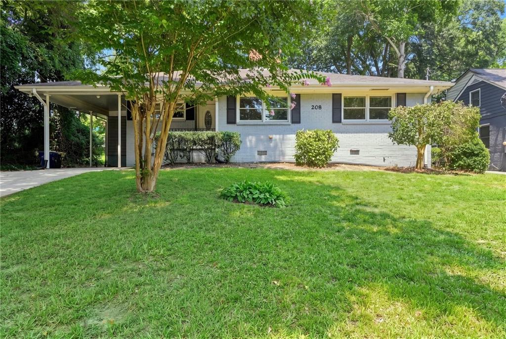 White brick ranch home with dark shutters, a covered carport, and a tree-shaded front lawn.