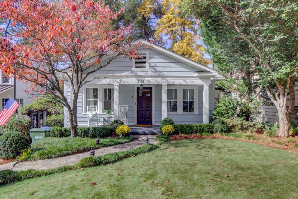 Gray house with white trim and dark door, framed by red and yellow autumn trees.
