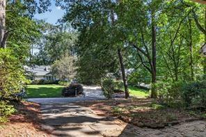 Curving driveway through a landscaped yard shaded by mature trees, with the house partly visible.