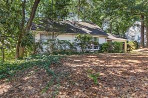 Single-story house among mature trees, viewed across a leaf-covered front yard.