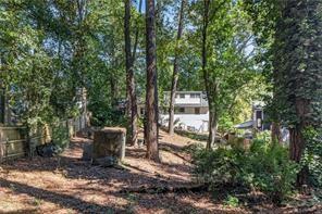 Wooded yard with mature trees and a house set back in the background.