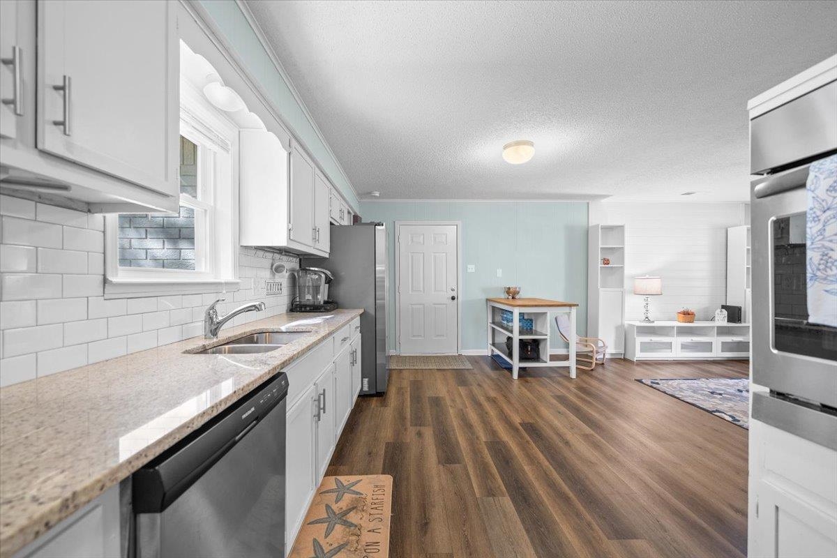 Kitchen with white cabinets, subway tile, stainless appliances, and an open living area.