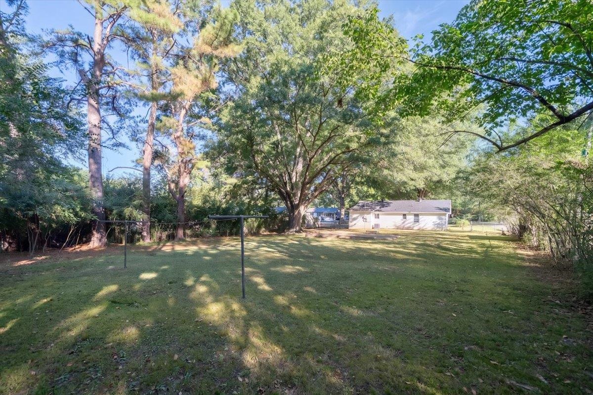 Tree-shaded backyard with a broad lawn and a small single-story house.
