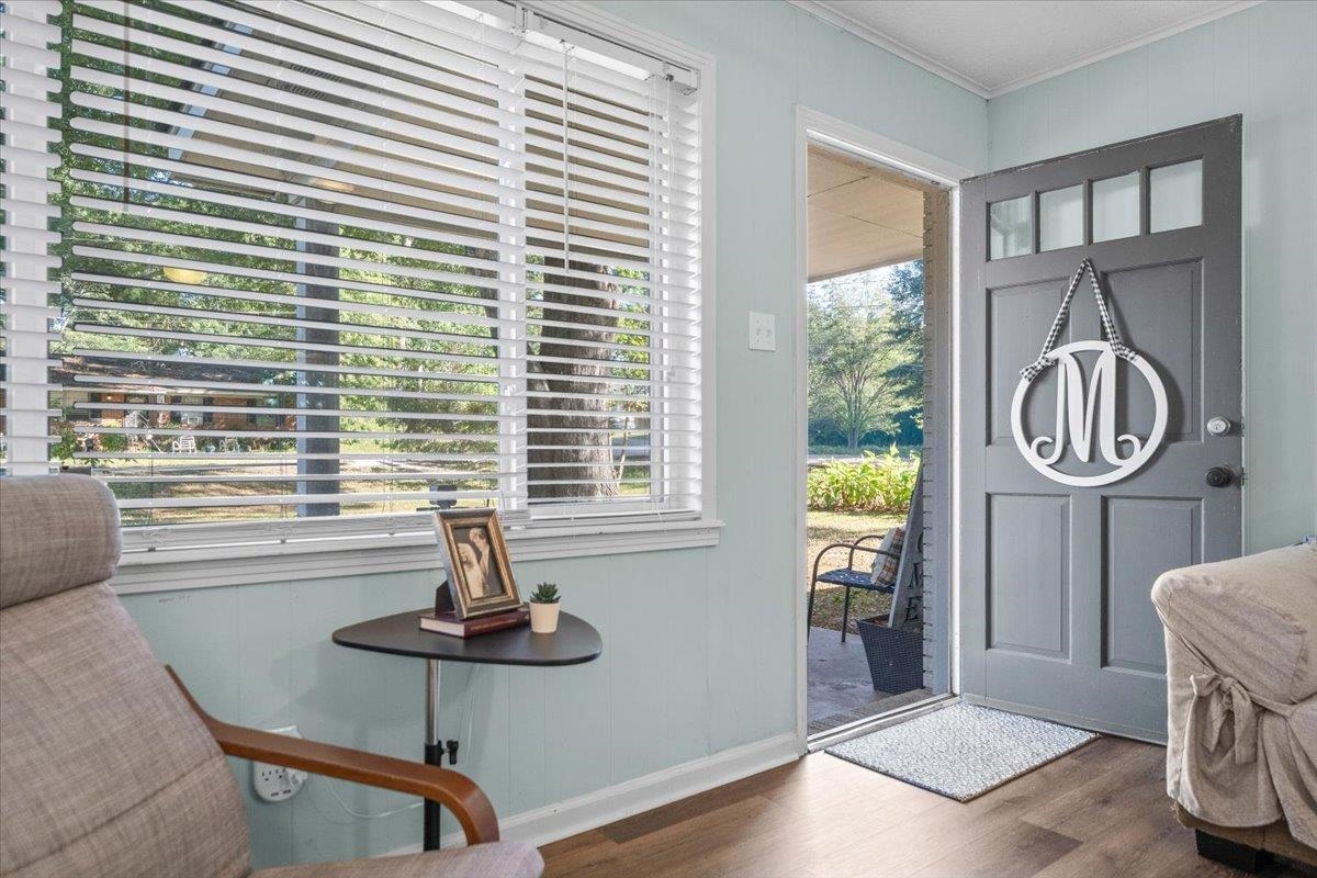 Sitting room with an open gray front door and large window with white blinds.