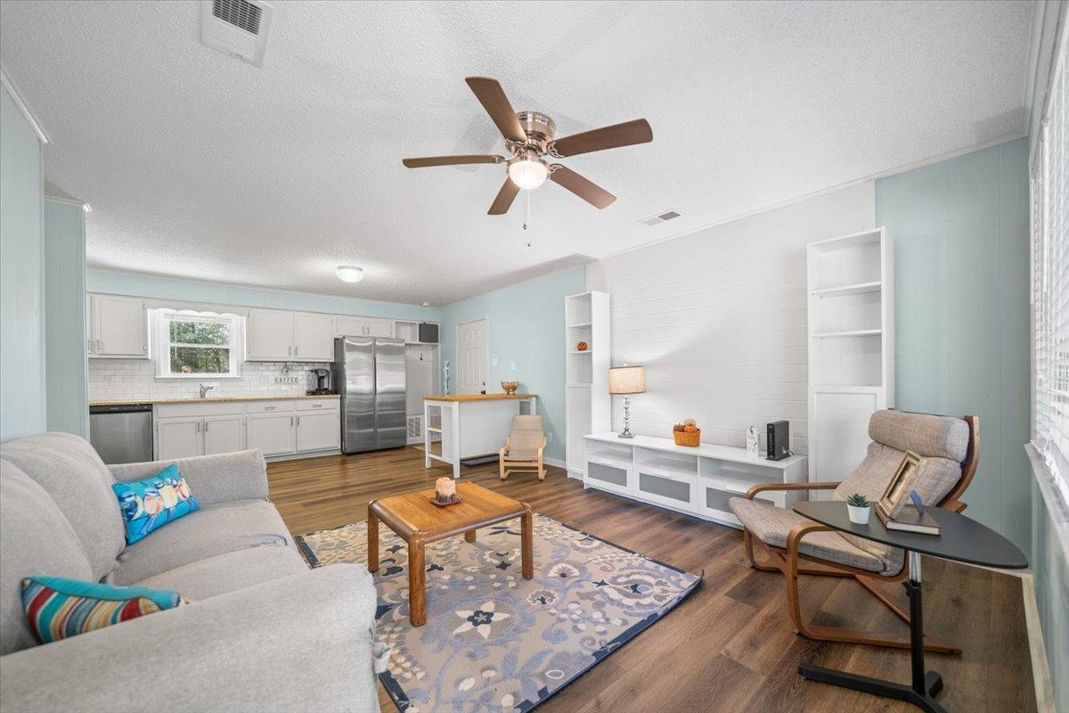 Open-plan living room and kitchen with wood floors, light cabinetry, and a ceiling fan.