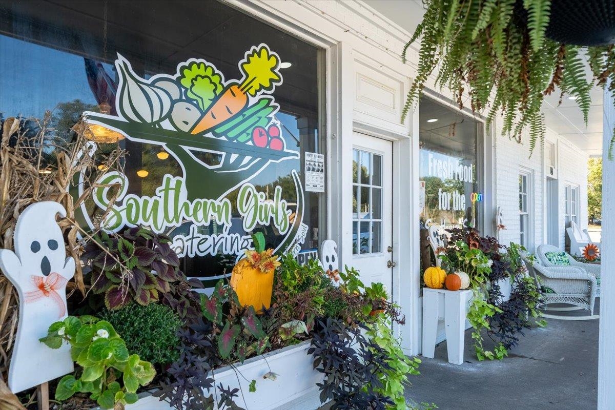 Storefront with Southern Girl’s Catering graphics, seasonal planters, and porch seating.