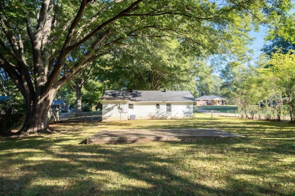 Single-story house behind a large shade tree, with a broad lawn and concrete patio.