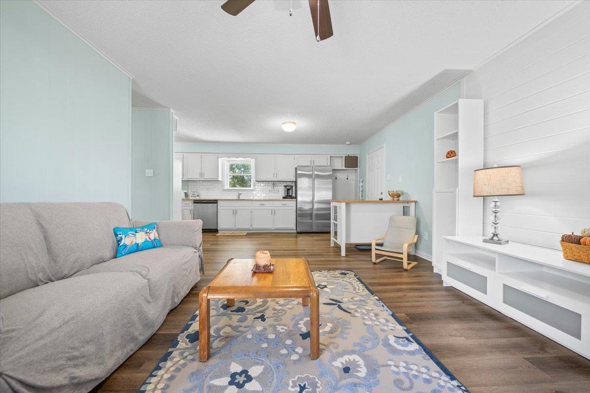 Living room opening to a white kitchen, with a gray sofa, patterned rug, and wood floors.
