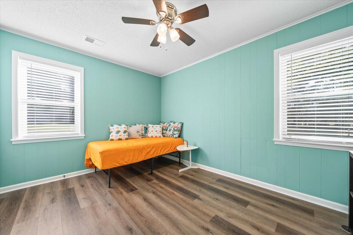 Bedroom with turquoise paneled walls, an orange-covered daybed, and two windows with blinds.