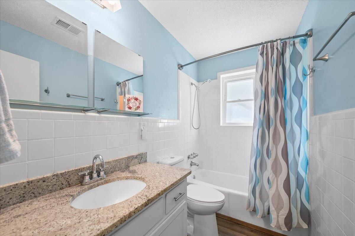 Bathroom with a granite vanity, white tile, and a patterned shower curtain.