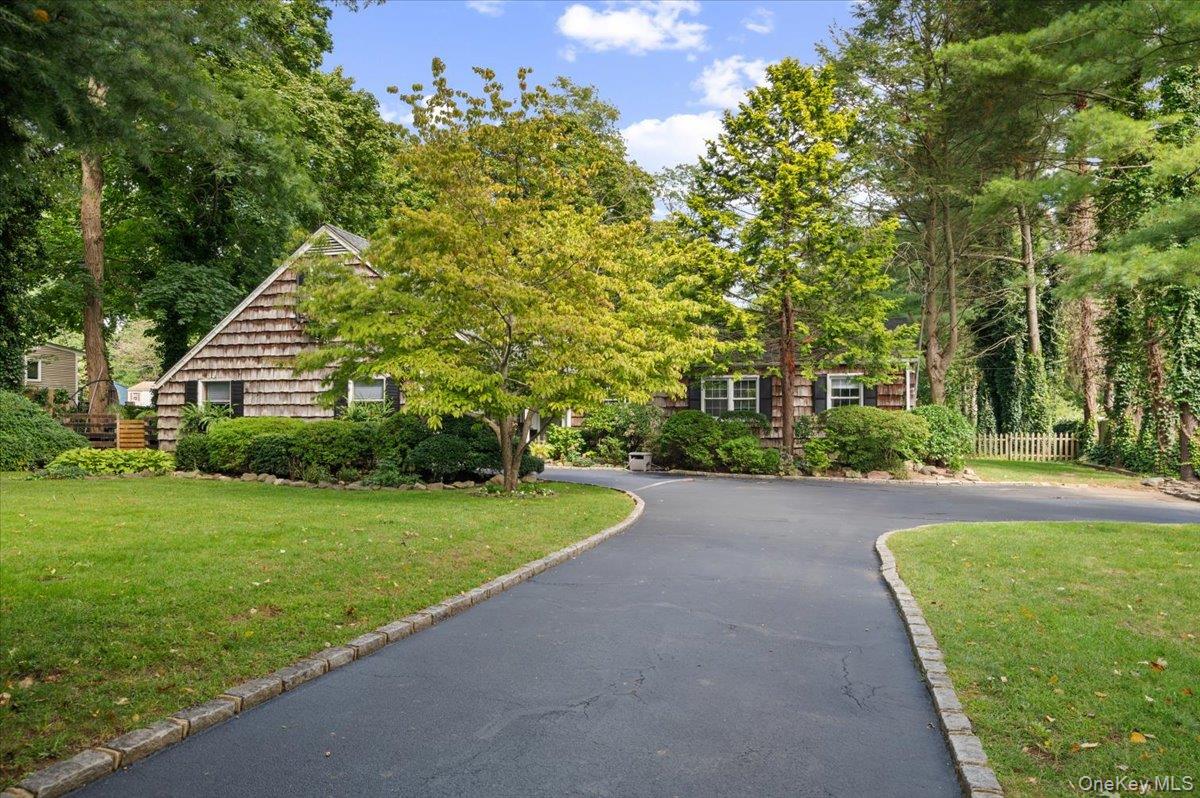 Cedar-shingle house framed by mature trees, with a curved driveway and landscaped lawn.