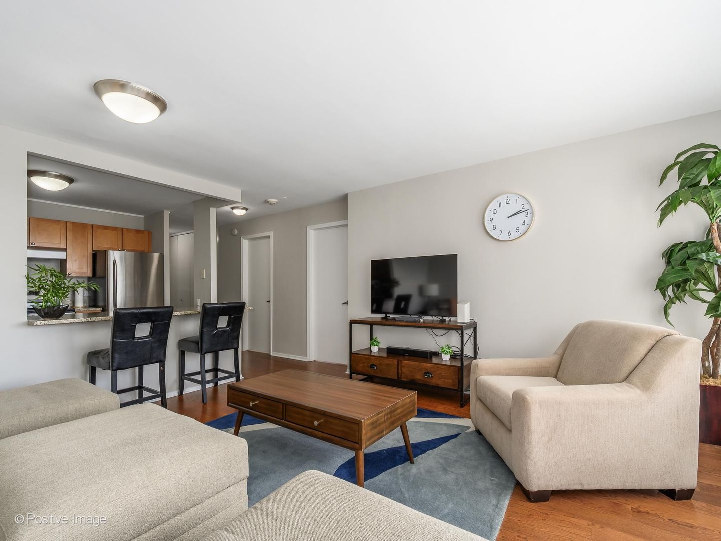 Condominium living room with a beige sofa, wood coffee table, and open kitchen breakfast bar.