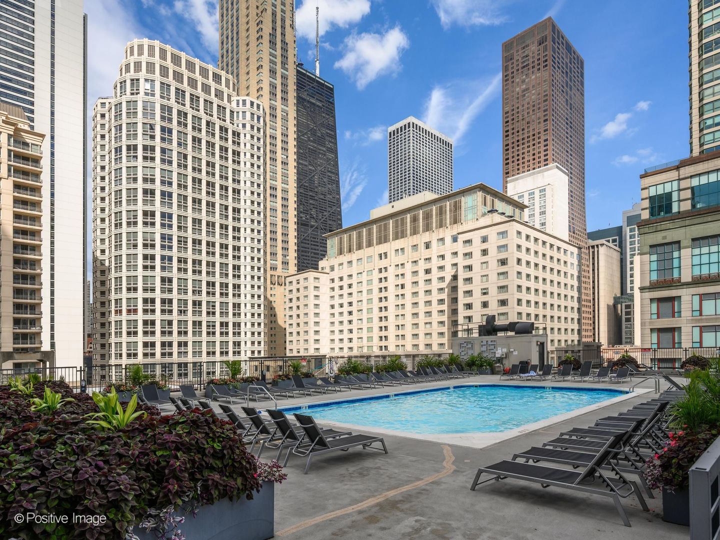 Rooftop pool with lounge chairs and landscaped planters, framed by downtown Chicago skyscrapers.