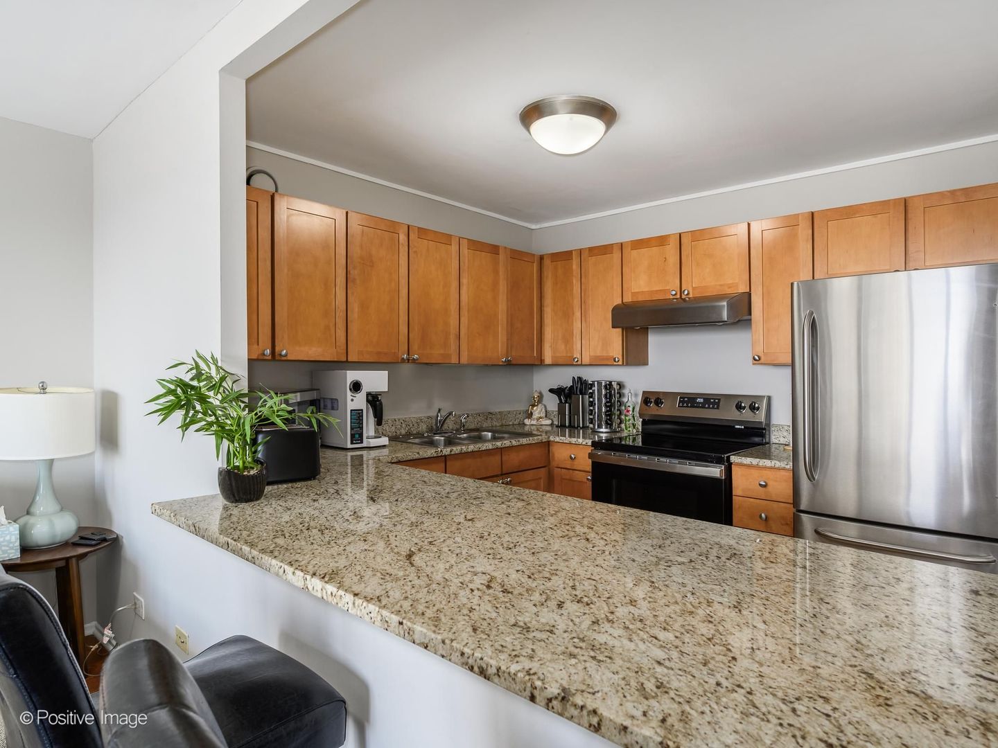 Condo kitchen with a granite peninsula, wood cabinets, and stainless steel appliances.