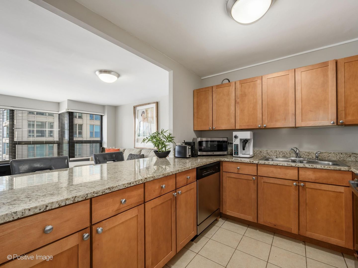 Condo kitchen with wood cabinets, granite counters, and large windows overlooking city buildings.